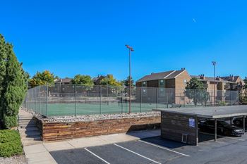 A tennis court is surrounded by a fence and a parking lot.